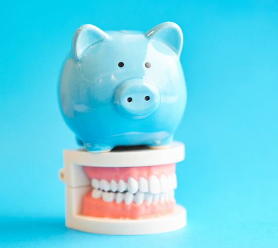 Piggy bank atop model teeth representing cost of teeth whitening in Lady Lake
