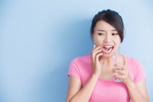 Woman in pink t-shirt wincing at teeth holding glass of water