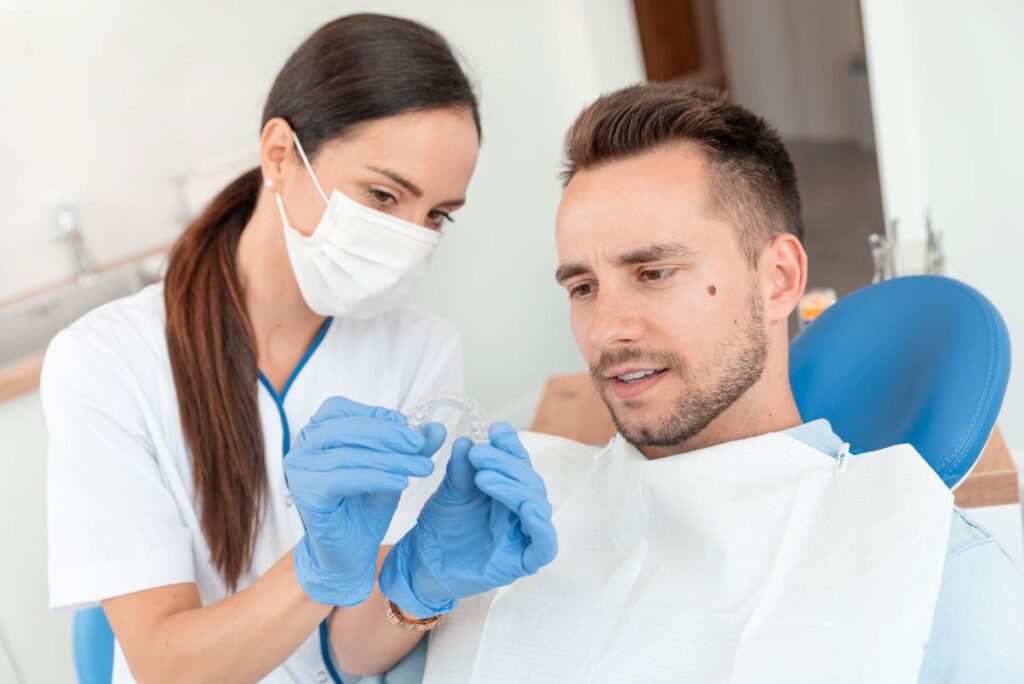 A dental assistant showing a male patient an Invisalign aligner.